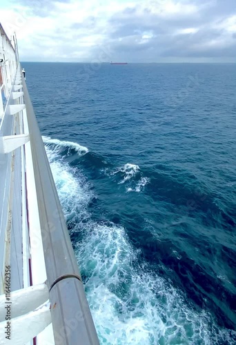 View of the side of a cruise ship in the open sea with waves crashing against its side in a deep blue tone with a cloudy sky on a summer day. Mention of family vacations and relaxation.