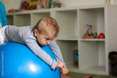 Portrait of a child with cerebral palsy on physiotherapy in a children therapy center. Boy with disability has therapy by doing exercises on fit ball. photo