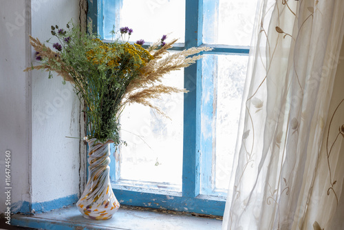 a bouquet of dried flowers in a vase on an old wooden windowsill