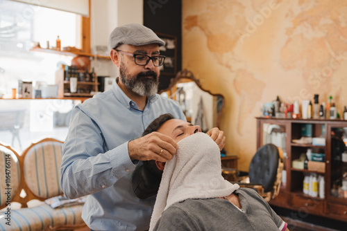 barbershop concept and people - Barber applies a hot towel to a man's beard. photo