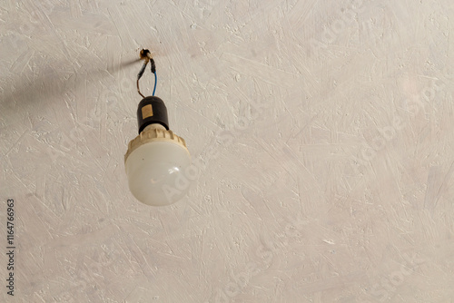 a dirty economy light bulb hangs on wires from the white ceiling