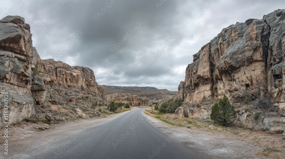 Empty asphalt road winding through rocky mountain cliffs, overcast sky 
