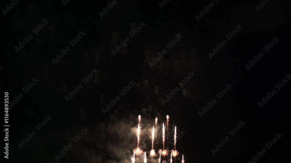 Brilliant red fireworks explode against a dark night sky, illuminating a cityscape below. Vibrant bursts and smoke create a festive, dynamic atmosphere, capturing the excitement of celebration.