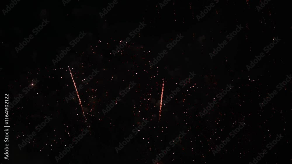 Brilliant red fireworks explode against a dark night sky, illuminating a cityscape below. Vibrant bursts and smoke create a festive, dynamic atmosphere, capturing the excitement of celebration.