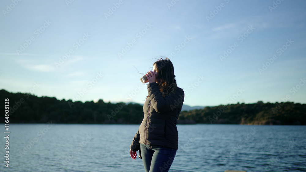 Woman drinking coffee by the lake at sunset enjoying nature Woman drinking coffee by the lake at sunset enjoying nature