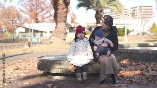 A Japanese parent and child, a 3-year-old girl, a 6-month-old baby boy, and a mother in her 30s, spend time in a lush park in Fukuoka City, Fukuoka Prefecture in the winter of December 2024.