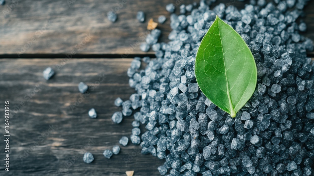Naklejka premium Natural black salt crystals with green leaf on wooden background, perfect for culinary use and healthy seasoning alternatives.