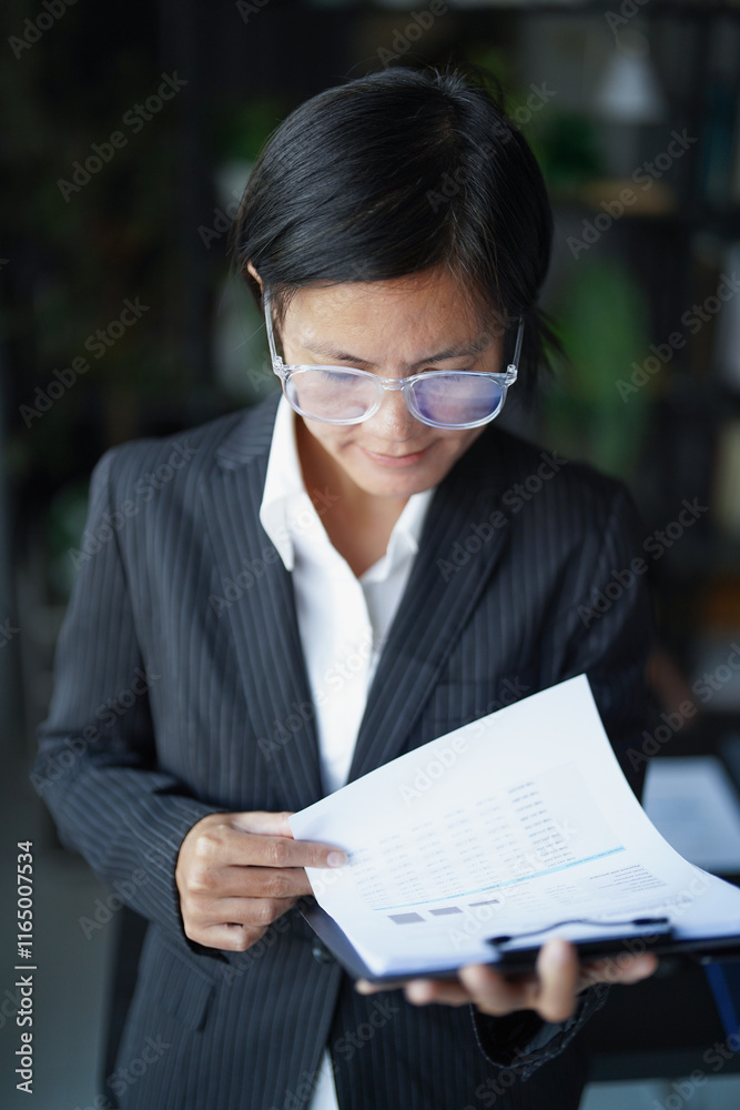 Asian businesswoman in suit standing reading documents Asian businesswoman in suit standing reading documents