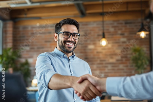A smiling man in eyeglasses and a blue shirt shakes hands in a modern office with a brick wall and warm lighting, depicting a positive business interaction. Ai generative