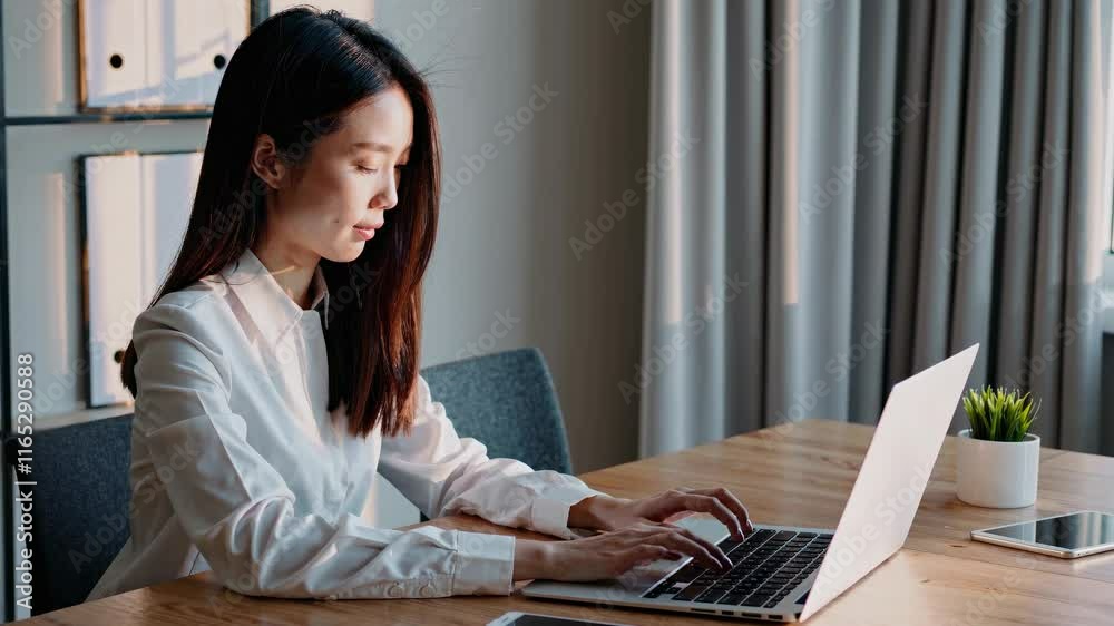 Young professional works on laptop in modern office setting during the day, focused and productive in a bright workspace