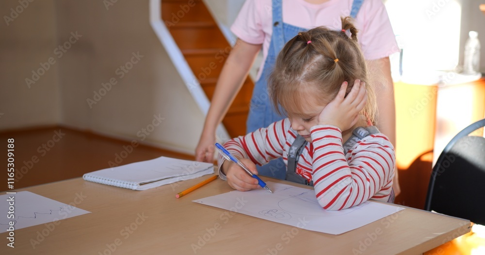 Young girl drawing intently, leaning head on hand, teacher assisting nearby, classmates watching creative process in kindergarten classroom. Concept teaching children to draw Young girl drawing intently, leaning head on hand, teacher assisting nearby, classmates watching creative process in kindergarten classroom. Concept teaching children to draw