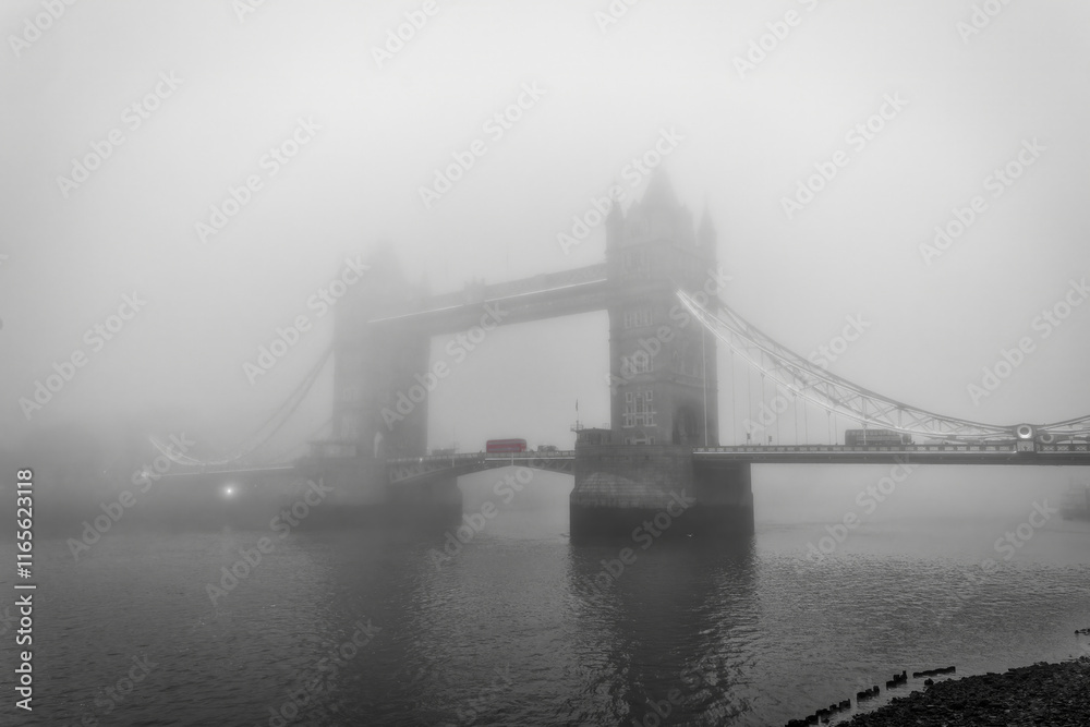 Moody view of the Tower Bridge of London, England, during a foggy autumn day with a red double decker bus on the bridge