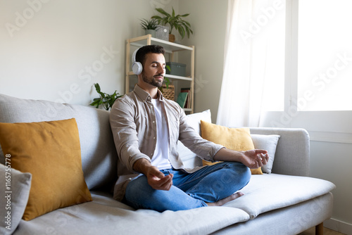 Man meditating on the couch listening to guided meditation using wireless headphones.