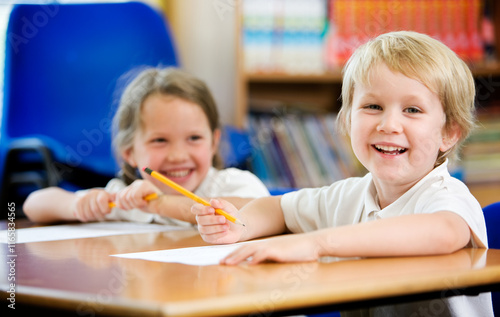 Elementary School: Candid and Carefree. A carefree and candid moment between a pair of young primary school friends sitting at their desk in the classroom.