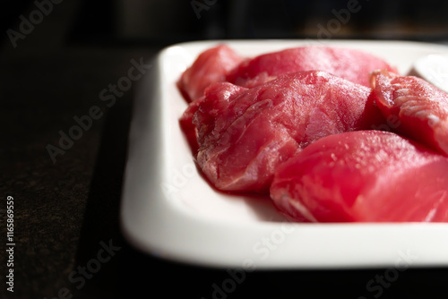 Sliced raw tuna fish on white rectangular plate on black table, fish steaks close-up photo