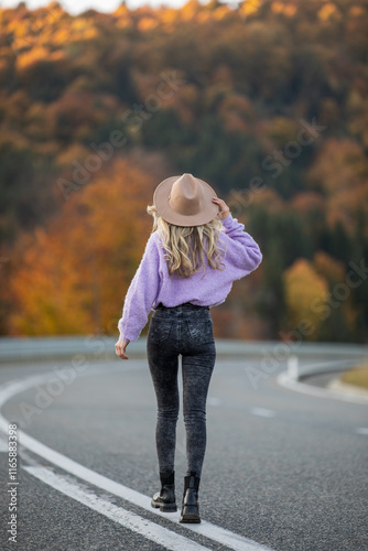 Obraz na płótnie A woman wearing a stylish outfit with a hat, walking along a road surrounded by colorful autumn trees in a picturesque forest. w salonie