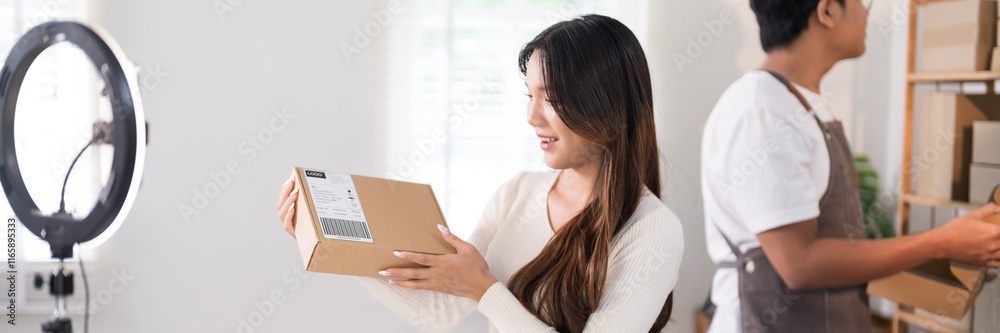 A woman enthusiastically livestreams while holding a box, showcasing her products with a ring light and laptop setup in a workspace filled with racks and packaging A woman enthusiastically livestreams while holding a box, showcasing her products with a ring light and laptop setup in a workspace filled with racks and packaging