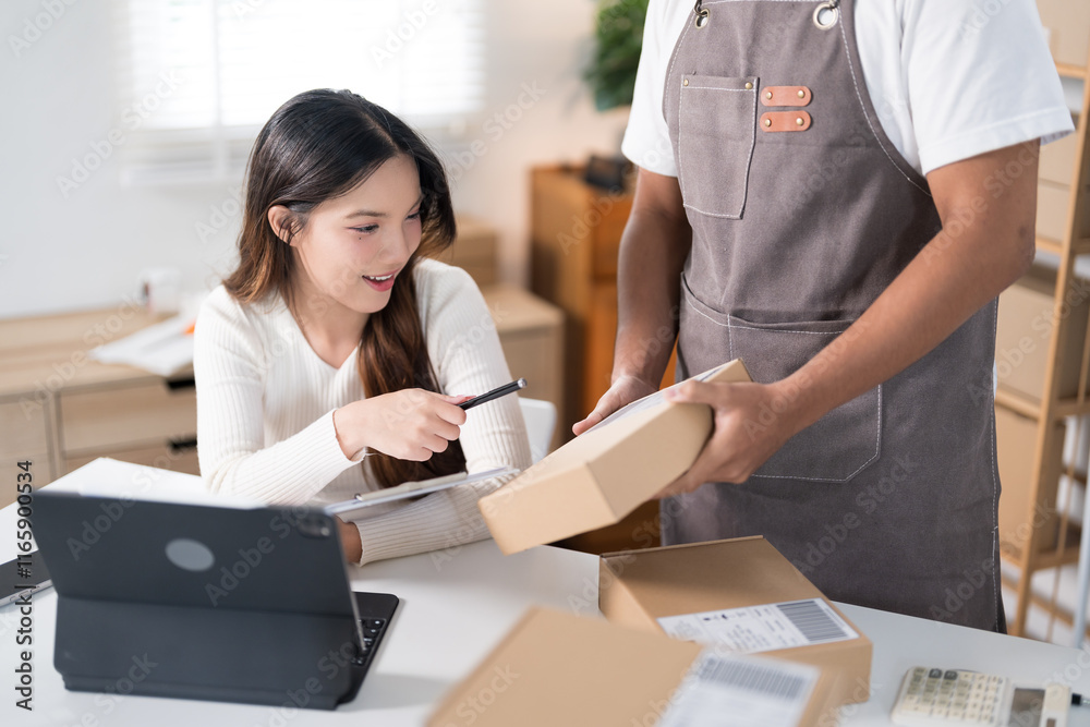 Obraz premium A man packs a box while a woman checks her phone in a workspace with clothing racks and shipping supplies