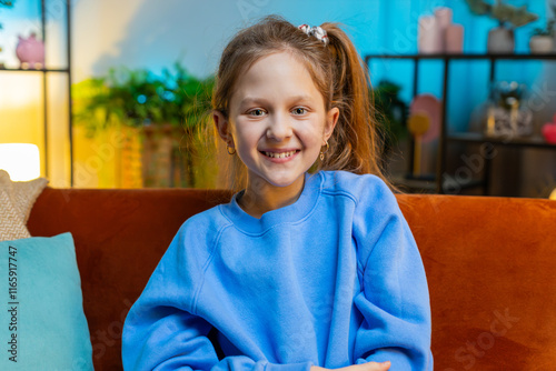 Close-up portrait of happy smiling Caucasian preteen school girl 10 years old. Young lovely child kid looking at camera at home night play room apartment sitting on orange couch. Ponytail hairstyle photo