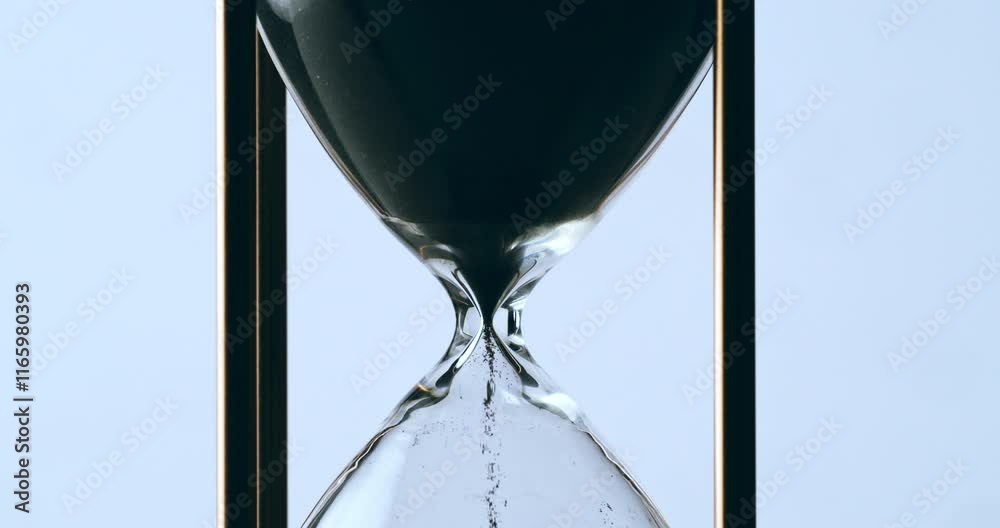 Super slow motion macro of fluid flow of black sand grains particles running inside hourglass sandglass clepsydra measuring passing time in countdown to deadline at 1000 fps.