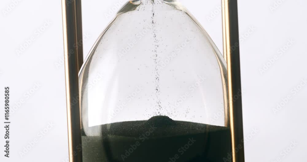Super slow motion macro of fluid flow of black sand grains particles running inside hourglass sandglass clepsydra measuring passing time in countdown to deadline at 1000 fps.