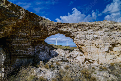Natural arch framing wind turbines in a sunny landscape