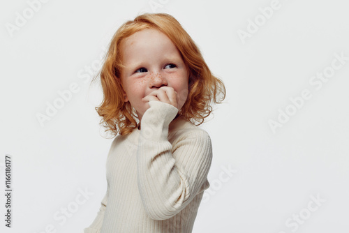 Redhaired girl posing in front of white background with hand near mouth, innocent beauty portrait photo