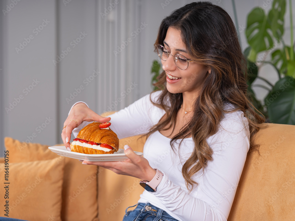 Eating croissant, beautiful young caucasian 20s woman eating croissant. Having breakfast at home. Happy female sitting at coach, joyful breakfast time cheat meal day concept idea image. Eating croissant, beautiful young caucasian 20s woman eating croissant. Having breakfast at home. Happy female sitting at coach, joyful breakfast time cheat meal day concept idea image.