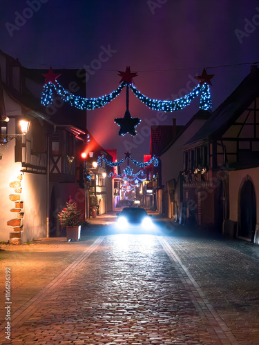 A picturesque street in Turckheim adorned with Christmas lights and decorations and a car with headlight in the middle, creating a magical holiday atmosphere photo