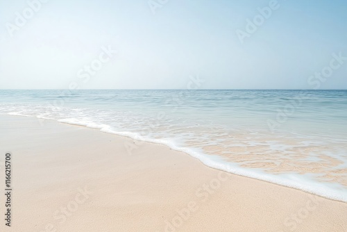 Fototapeta Naklejka Na Ścianę i Meble -  Tranquil beach scene shows soft waves gently washing ashore on light beige sandy beach. Calm ocean water meets clear sky. Peaceful, serene summer vacation ambiance. Ideal for relaxation, rest.