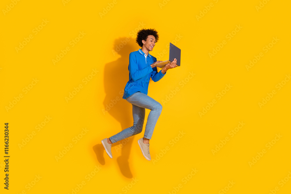 Full length photo of handsome young guy running hold netbook dressed stylish blue garment isolated on yellow color background Full length photo of handsome young guy running hold netbook dressed stylish blue garment isolated on yellow color background