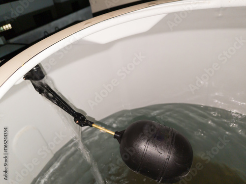 A water tank is filling with water. A black float can be seen