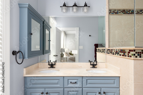 A bathroom with blue cabinet and medicine cabinet, a marble countertop, tiled shower, and view towards the primary bedroom.