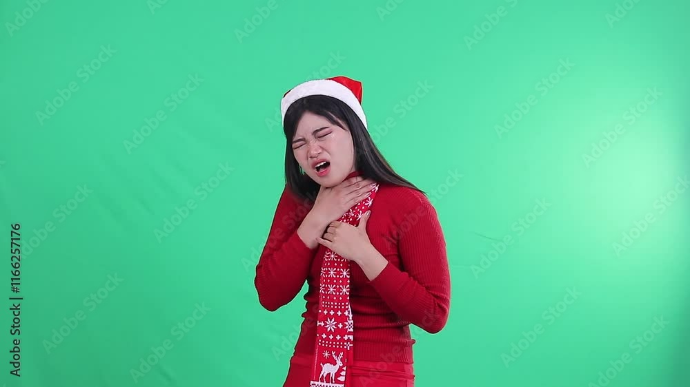 indonesia woman showing pain expression on neck while appearing to have difficulty swallowing wearing Christmas sweater, Santa hat and scarf, on green screen indonesia woman showing pain expression on neck while appearing to have difficulty swallowing wearing Christmas sweater, Santa hat and scarf, on green screen