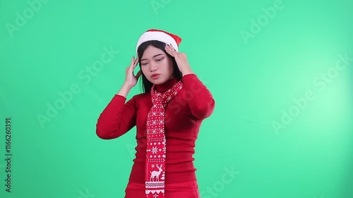 charm of Asian woman wearing christmas sweater, Santa hat and scarf, her head is dizzy weak both hands hold her head hurt, isolated on green background, green screen