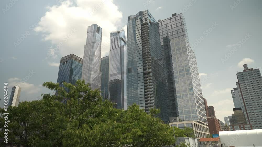 A view of tall, glass-covered skyscrapers in Manhattan, showcasing modern architecture. Trees and urban structures are visible in the foreground under a sunny sky. A view of tall, glass-covered skyscrapers in Manhattan, showcasing modern architecture. Trees and urban structures are visible in the foreground under a sunny sky.