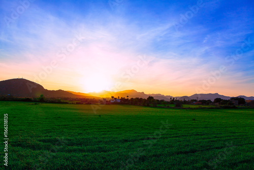 Sunset over Mallorca island. Lush green field with hills in the background and a vibrant sunrise or sunset casting a warm glow across the sky