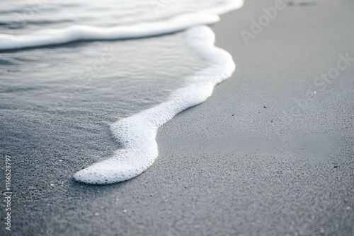 Serene coastal scene close-up of a gentle wave receding on a sandy beach, showcasing the tranquil beauty of the ocean meeting the shore.