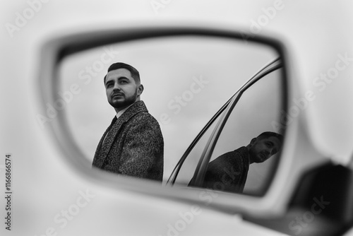 reflection of a man in the side mirror of a car. The man is wearing a coat and looking to the side, turning his head slightly. photo