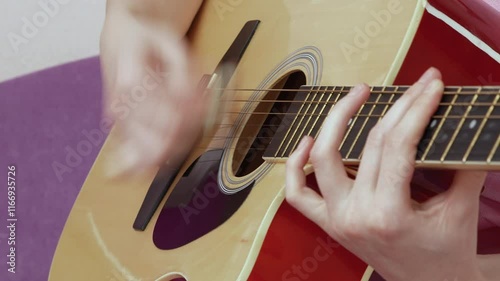 Close-up view of female guitarist is performing captivating solo, deftly manipulating fingers over frets and neck of acoustic guitar. This performance, executed in strumming style with guitar pick