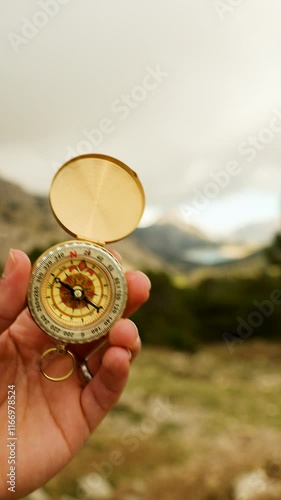 Vertical video of male hand holding a compass on the mountain with grey clouds in the background, orientation in nature