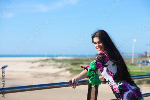 Latin woman, young and beautiful, dancing flamenco with her hair in the air on the railing. On the horizon the Atlantic Ocean. Woman in white dress with ruffles and flowers typical of andalusia. photo