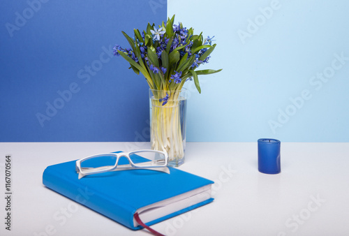 Obraz na płótnie Blue notebook, glasses, candle and snowdrops on white and pastel blue background in studio w salonie