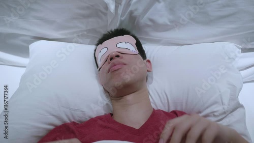 A young man is lying comfortably in bed wearing a sleep mask. The serene environment promotes relaxation and a restful night's sleep, highlighting the importance of self-care and proper sleep hygiene 