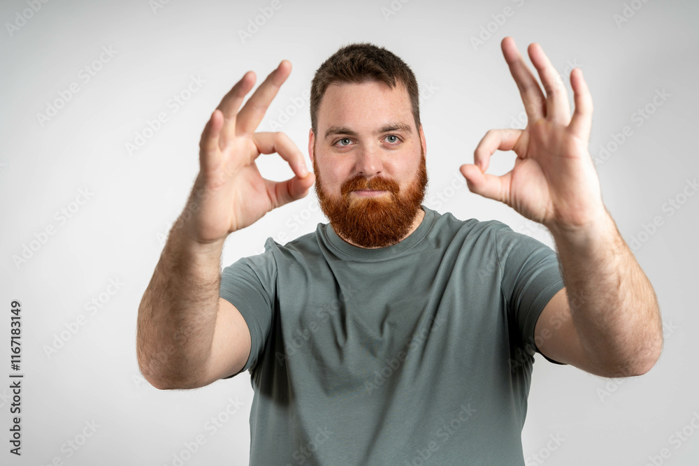 Young handsome man with beard wearing casual t-shirt over grey background doing happy thumbs up gesture with hand. Approving expression looking at the camera showing success. Young handsome man with beard wearing casual t-shirt over grey background doing happy thumbs up gesture with hand. Approving expression looking at the camera showing success.