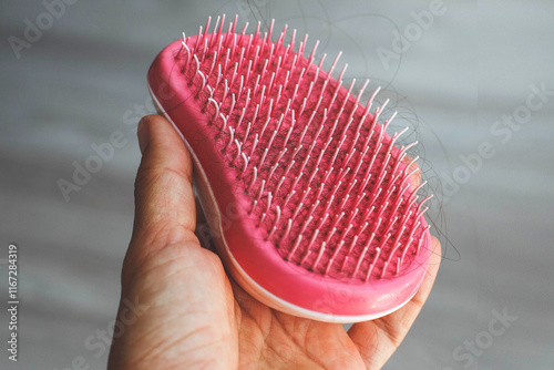 pink modern hairbrush in female hand with dark hair on comb, close up photo