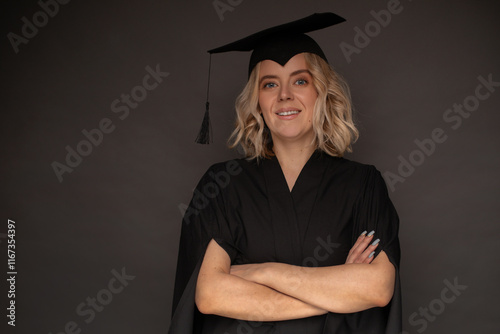 Smiling woman in a black graduation cap and gown with arms crossed, celebrating academic achievement. Studio portrait on a neutral background, symbolizing success, education, and accomplishment. photo