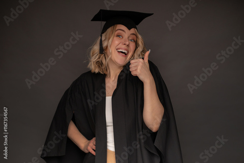 A joyful female graduate in a black cap and gown gives a thumbs-up gesture, expressing excitement and pride. Ideal for education, success, and graduation-themed visuals. photo