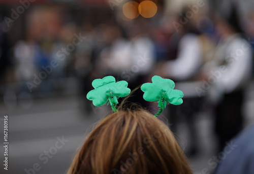 A spectator with her back turned and wearing a shamrock headband watches the St. Patrick's Day parade photo