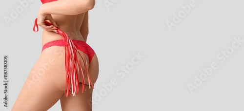 Young woman in sexy lingerie holding whip on grey background with space for text, closeup